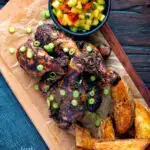 Overhead Jamaican jerk chicken drumsticks with potato wedges and mango salsa featuring a title overlay.