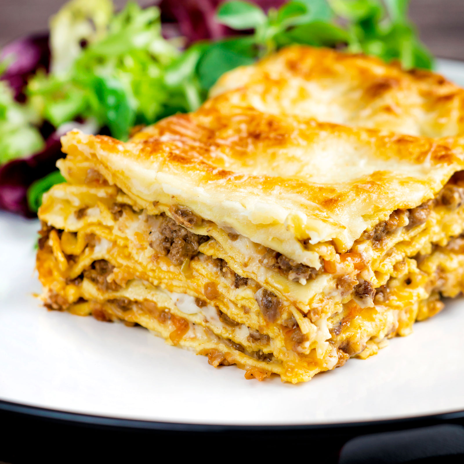 Perfectly layered lasagna bolognese with a crispy cheesy topping served with a side salad.