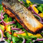 Pan fried jerk salmon fillet served with mango and rocket salad featuring a title overlay.