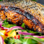 Close up pan fried jerk salmon fillet served with mango and rocket salad.