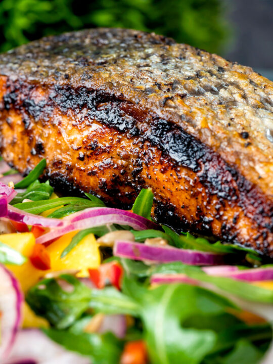 Close up pan fried jerk salmon fillet served with mango and rocket salad.