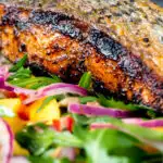 Close up pan fried jerk salmon fillet served with mango and rocket salad featuring a title overlay.