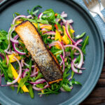 Overhead pan fried jerk salmon fillet served with mango and rocket salad featuring a title overlay.