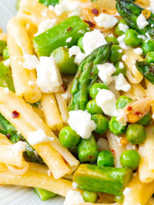 Close up pea and asparagus pasta with casarecce, feta cheese and chilli flakes.