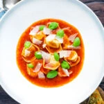 Overhead store bought tortellini soup with tomato, fresh basil and parmesan shavings.