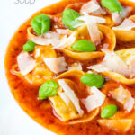 Close up store bought tortellini soup with tomato, fresh basil and parmesan shavings featuring a title overlay.
