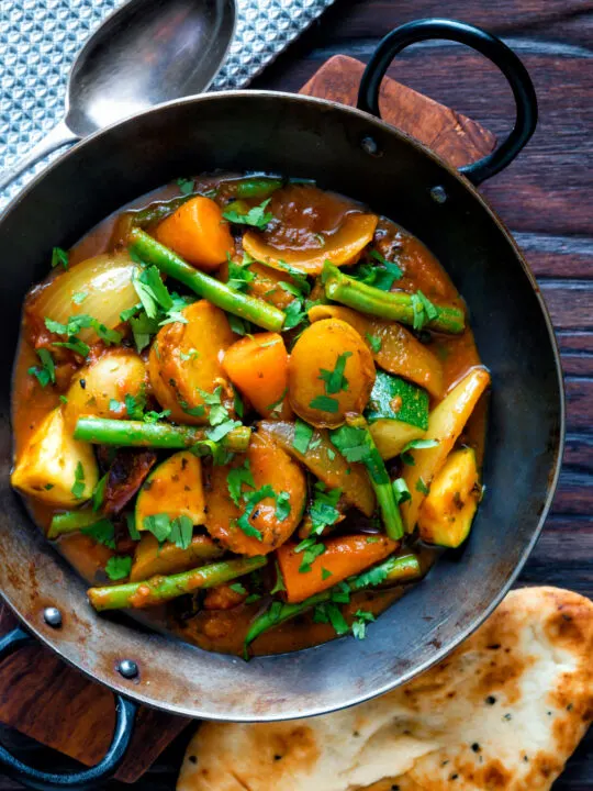 Overhead vegan mixed vegetable karahi curry served in an iron kadai.