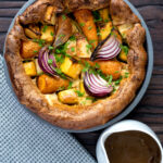 Overhead roasted vegetable toad in the hole with a jug of vegetarian onion gravy.