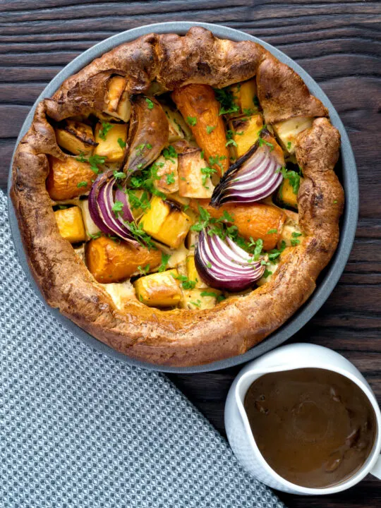 Overhead roasted vegetable toad in the hole with a jug of vegetarian onion gravy.