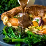 Roasted vegetable toad in the hole having vegetarian onion gravy poured over it.