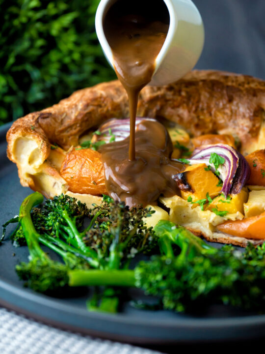 Roasted vegetable toad in the hole having vegetarian onion gravy poured over it.