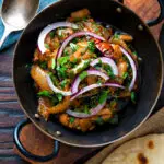 Overhead achari chicken or chicken pickle served in a kadai with a chapati.