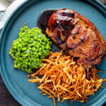 Over head pan fried Barnsley chop with port lamb sauce, straw potatoes and minted peas featuring a title overlay.