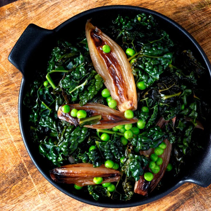 Overhead Braised cavolo nero kale with peas and shallots in a black bowl.