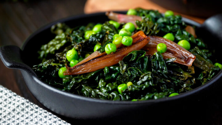 Braised cavolo nero kale with peas and shallots in a black bowl.