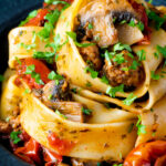 Close up chorizo pasta with pappardelle, tomatoes and mushrooms featuring a title overlay.