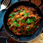 Overhead lamb bhuna curry served in an iron karahi with naan bread.