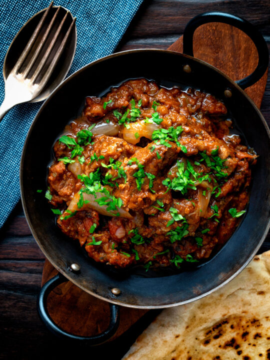 Overhead lamb bhuna curry served in an iron karahi with naan bread.