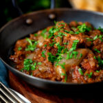 Lamb bhuna curry served in an iron karahi with naan bread.