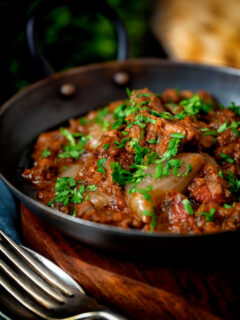 Lamb bhuna curry served in an iron karahi with naan bread.