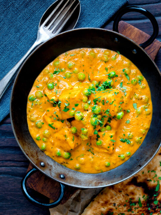 Overhead matar paneer curry served in an iron kadai with fresh coriander.