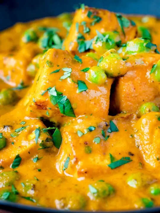 Close up matar paneer curry served in an iron kadai with fresh coriander.