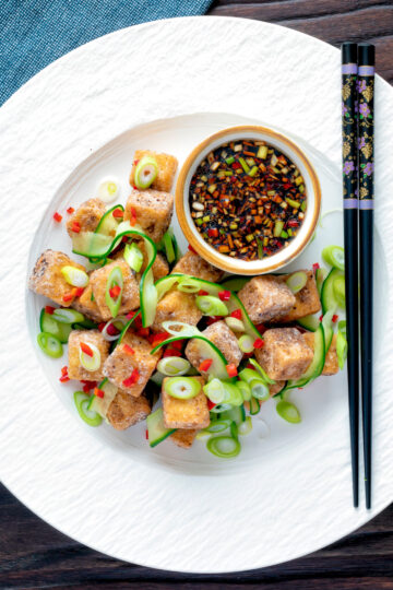 Overhead salt and pepper tofu with a chilli soy dipping sauce and pickled cucumber.