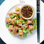 Overhead salt and pepper tofu with a chilli soy dipping sauce and pickled cucumber featuring a title overlay.