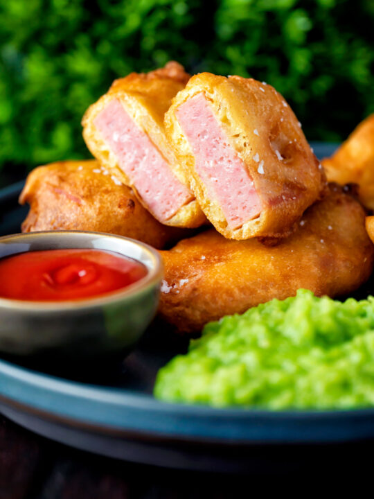 Cut open spam fritters served with mushy peas and ketchup.