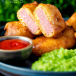 Cut open spam fritters served with mushy peas and ketchup featuring a title overlay.