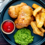 Overhead crispy spam fritters served with chips, mushy peas and ketchup.