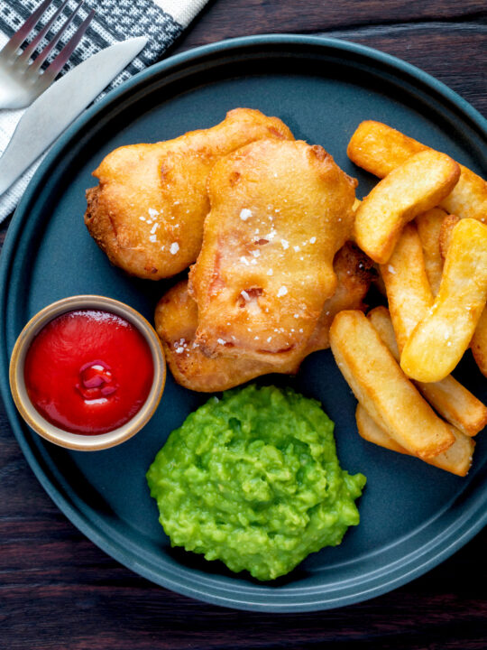 Overhead crispy spam fritters served with chips, mushy peas and ketchup.