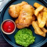 Overhead crispy spam fritters served with chips, mushy peas and ketchup featuring a title overlay.