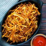 Overhead straw or matchstick potatoes served in a bowl with tomato ketchup.