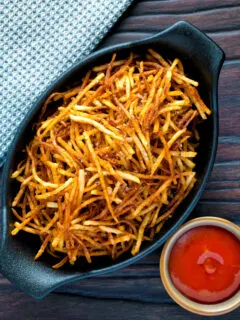 Overhead straw or matchstick potatoes served in a bowl with tomato ketchup.