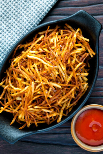 Overhead straw or matchstick potatoes served in a bowl with tomato ketchup.