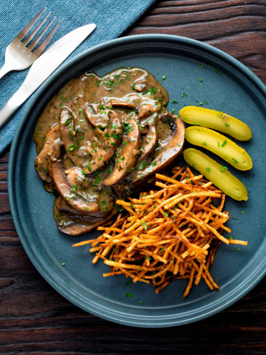 Overhead vegan mushroom stroganoff served with pickles and straw potatoes.