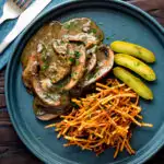 Overhead vegan mushroom stroganoff served with pickles and straw potatoes featuring a title overlay.