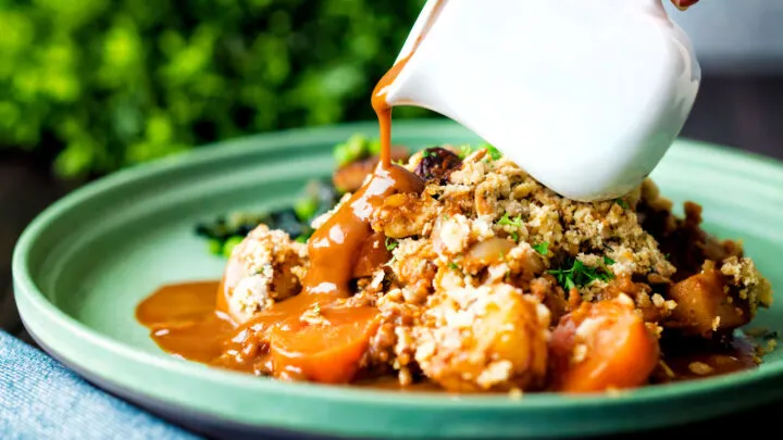 Vegan onion gravy being poured over a vegetable crumble.