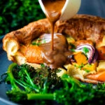 Vegan onion gravy being poured over a vegetable toad in the hole.