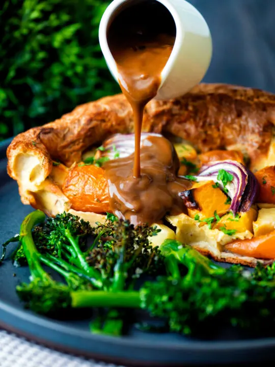 Vegan onion gravy being poured over a vegetable toad in the hole.