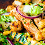 Close up warm chicken and mango salad with croutons and red onion.