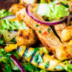 Close up warm chicken and mango salad with croutons and red onion featuring a title overlay.