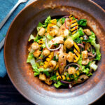 Overhead warm chicken and mango salad with croutons and red onion.
