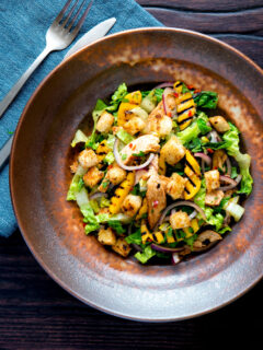 Overhead warm chicken and mango salad with croutons and red onion.