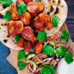 Overhead Amritsari fish pakora served with chapatis, chunky kachumber salad and raita featuring a title overlay.