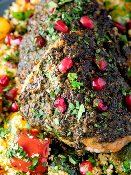 Close up chermoula chicken thighs served with roasted vegetable couscous and fresh herbs.