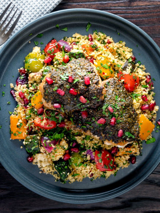 Overhead chermoula chicken thighs served with roasted vegetable couscous and fresh herbs.