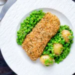 Overhead baked cod loin in crispy panko breadcrumbs with crushed minted peas and potatoes.