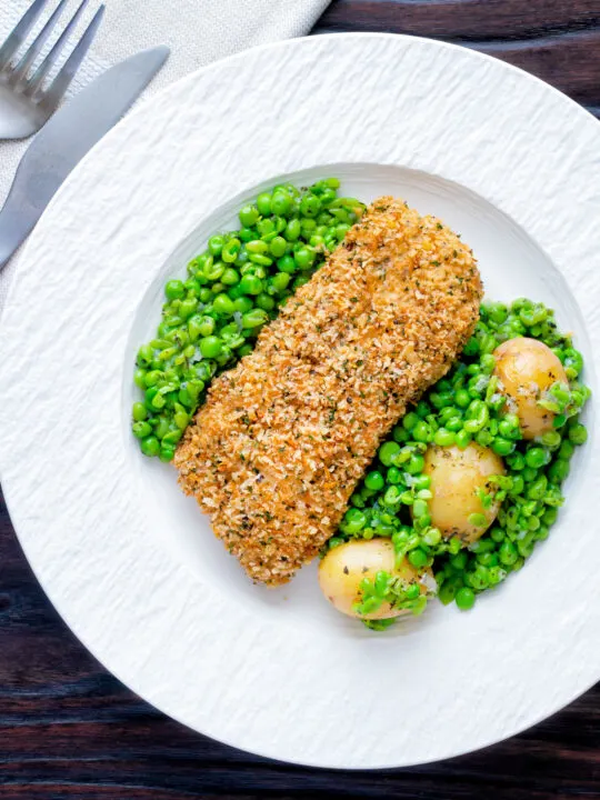 Overhead baked cod loin in crispy panko breadcrumbs with crushed minted peas and potatoes.